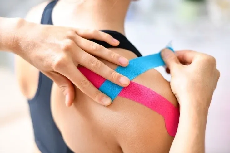 A person is taping their shoulder with colored tape.